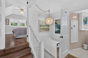 A staircase leading to a bedroom with a bed, a ceiling fan, and artwork on the walls. - Downtown Rehoboth Beach House Quick Walk to Beach Pets Permitted (Rehoboth Beach)