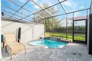A covered outdoor swimming pool with a chair, surrounded by a glass enclosure, and a view of a residential area. - Private Pool | No Carpet | Walk to Walmart | Spotless (Kissimmee)
