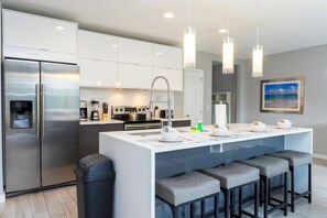 A modern kitchen with a central island, stainless steel appliances, and pendant lighting. - Private Pool | No Carpet | Walk to Walmart | Spotless (Kissimmee)