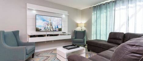 Una sala de estar con televisor de pantalla plana, un sofá, una silla y una mesita de centro.