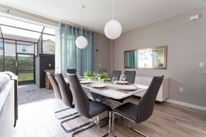 A dining area with a table set for four, surrounded by chairs, in a room with a large window and a mirror on the wall. - Private Pool | No Carpet | Walk to Walmart | Spotless (Kissimmee)