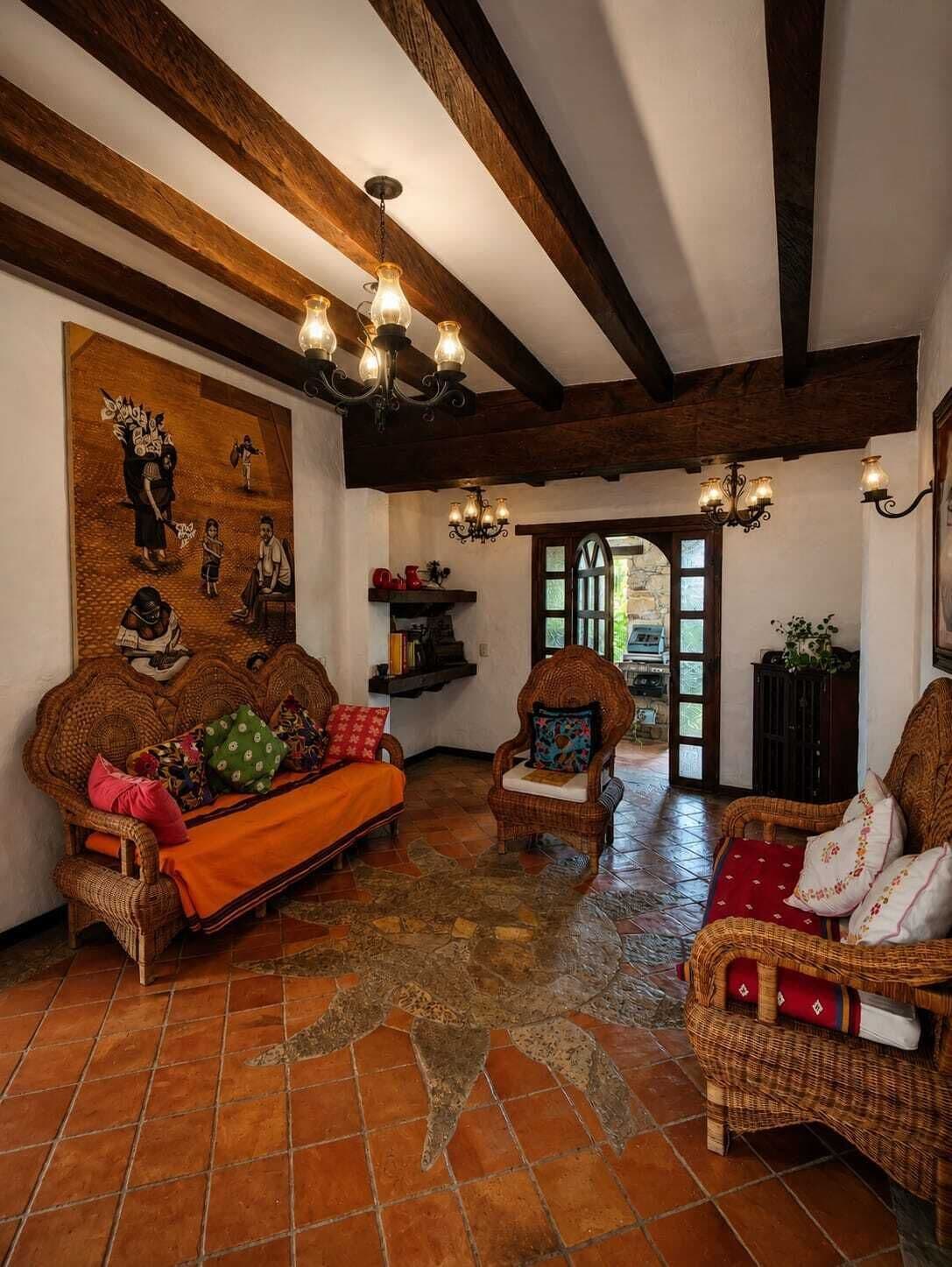 Una habitación tradicional con vigas de madera a la vista, un sofá grande de fibras naturales, un sillón más pequeño y un tapiz estampado.