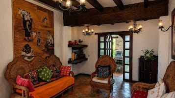Una habitación tradicional con vigas de madera a la vista, un sofá grande de fibras naturales, un sillón más pequeño y un tapiz estampado.
