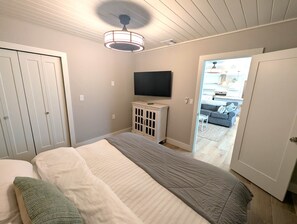 A bedroom with a bed, a television on a cabinet, and a view of a living area through an open door. - Sea Glass Retreat (Manasota Key)
