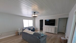 Un salon spacieux avec un canapé gris, un téléviseur à écran plat et un ventilateur de plafond.