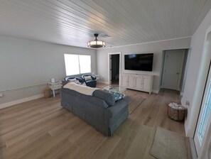 Ein geräumiges Wohnzimmer mit grauem Sofa, Flachbildfernseher und Deckenventilator.