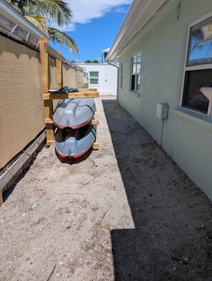 A narrow outdoor pathway with a boat on a wooden stand, a building with a white exterior, and a clear sky. - Sea Glass Retreat (Manasota Key)
