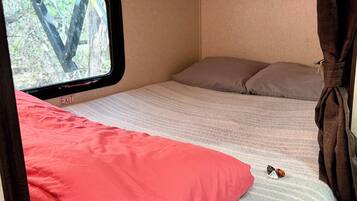A compact RV interior with a bed, a window, and a curtain.