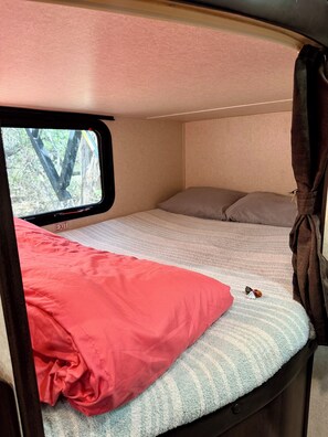 Interior compacto de una autocaravana con cama, ventana y cortina.