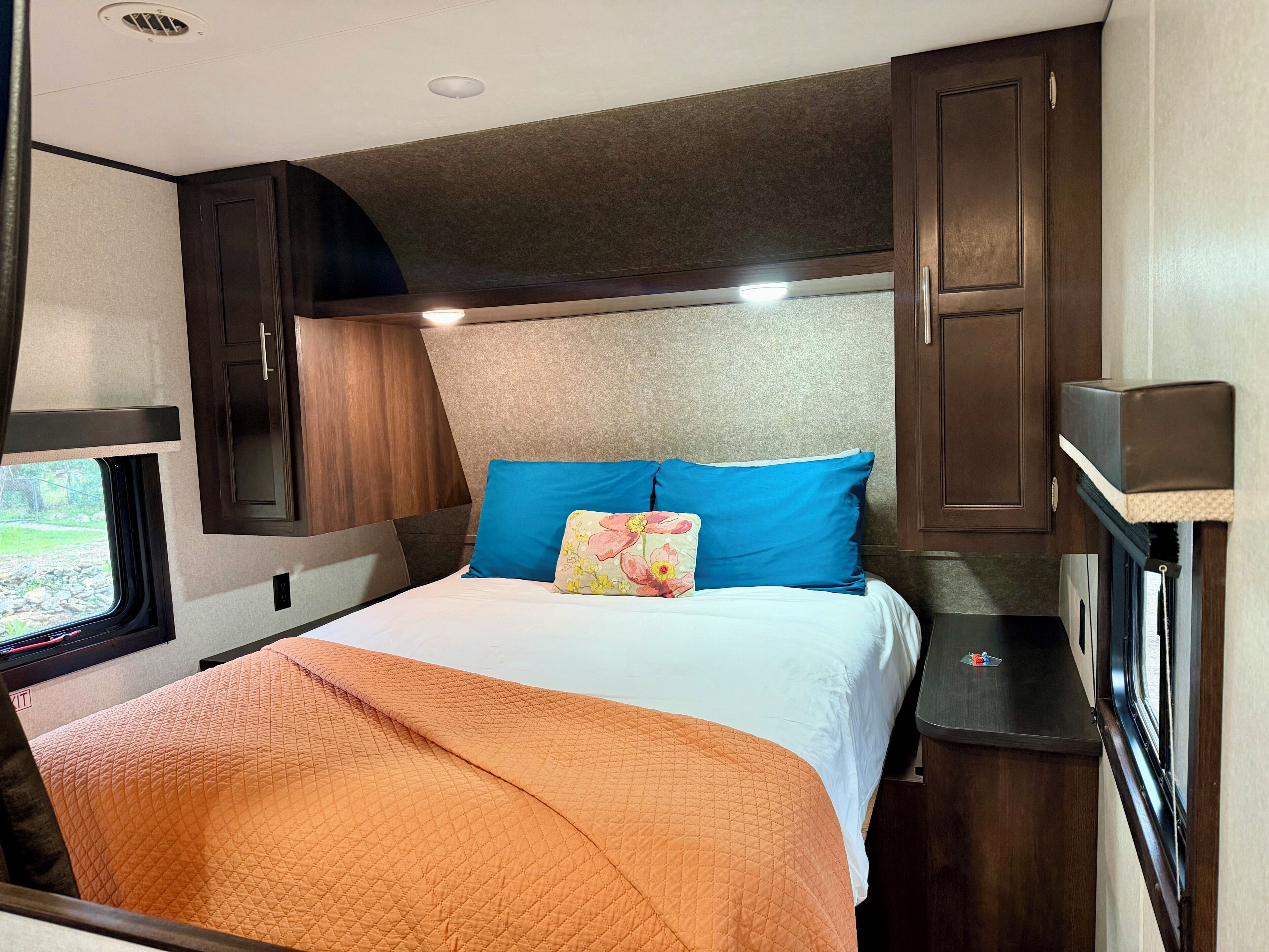 A compact RV interior with a bed, a window, and built-in cabinets.