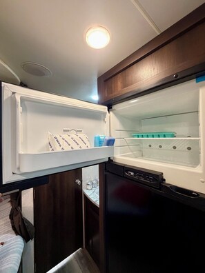 An open refrigerator with a freezer compartment on top, a water dispenser, and a built-in ice maker.