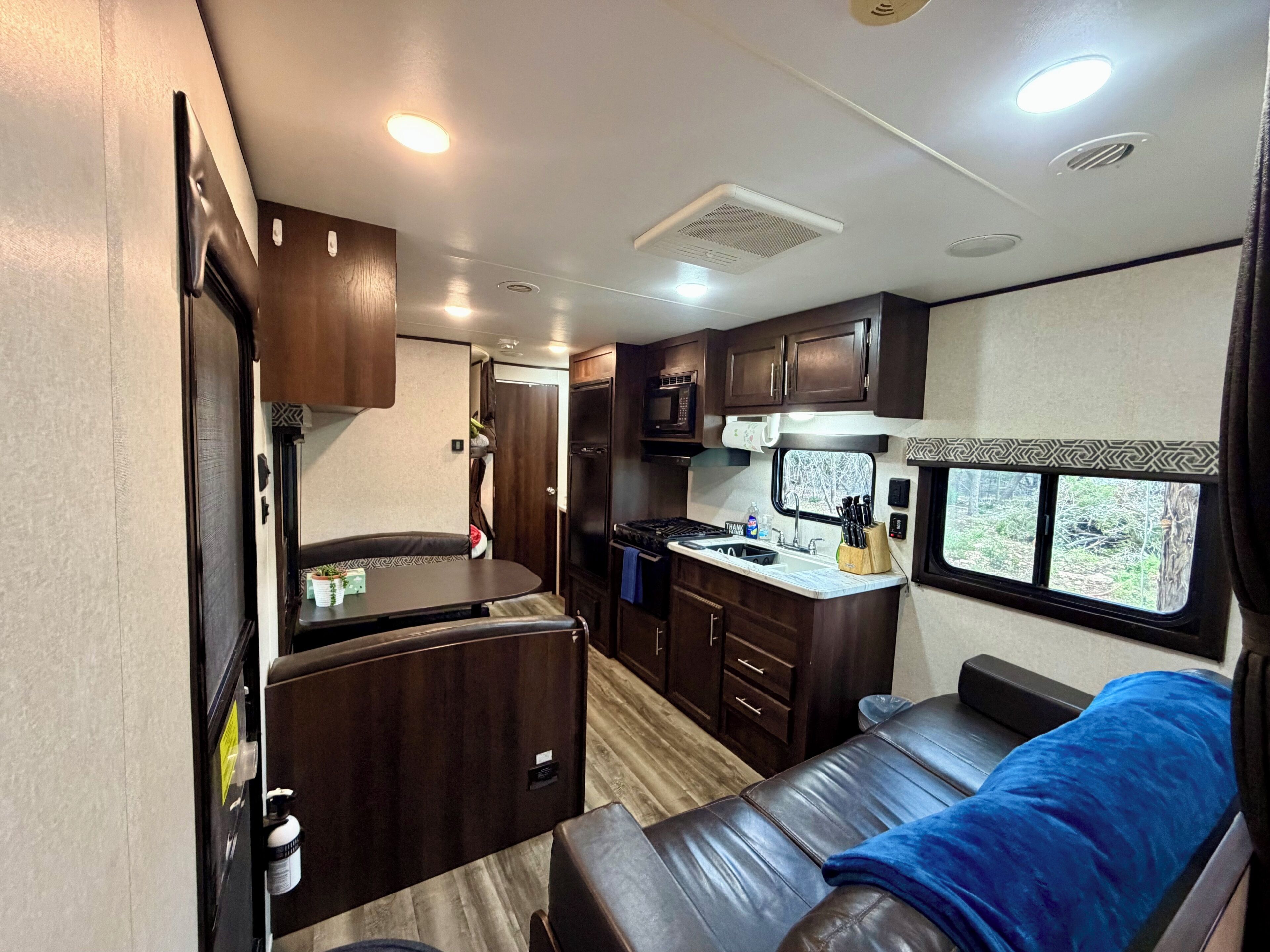 A compact RV interior with a kitchenette, a dining area, and a sleeping space.