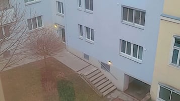 A multi-story building with a flat facade, multiple windows, and a small courtyard with steps leading to the entrance.