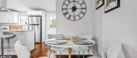 A modern kitchen with white cabinets, a stainless steel refrigerator, and a dining area with a round table and white chairs.