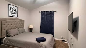 A bedroom with a bed, a ceiling fan, a wall-mounted TV, and a framed picture.