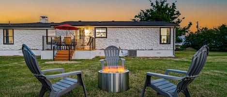 A house with a stone exterior, a fire pit in the yard, and two chairs facing the fire.