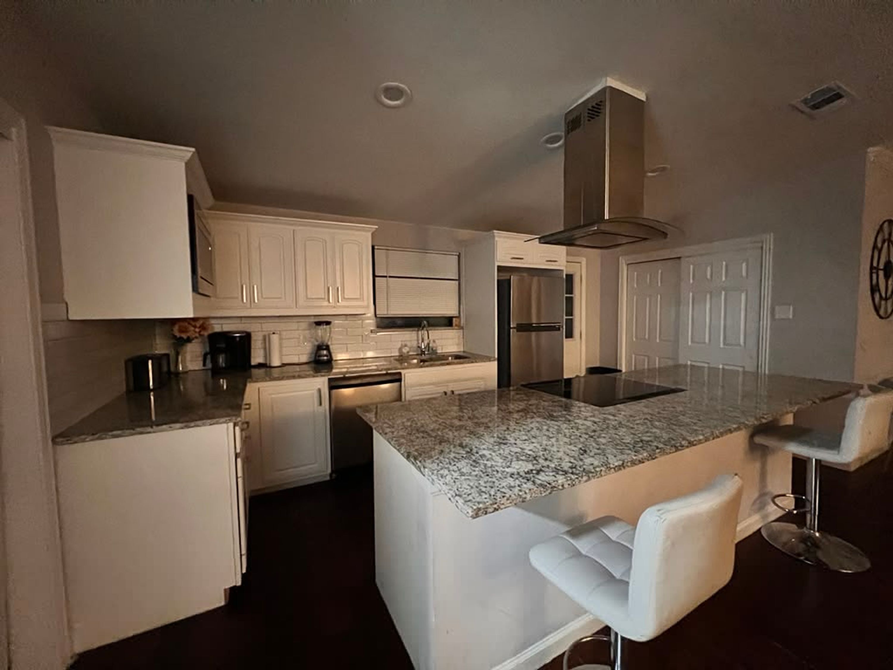 A modern kitchen with white cabinetry, a granite countertop, a built-in island with bar stools, and stainless steel appliances.