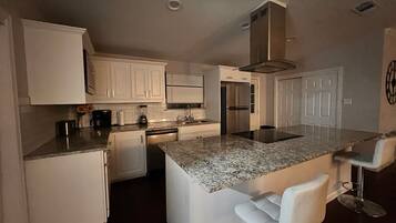 A modern kitchen with white cabinetry, a granite countertop, a built-in island with bar stools, and stainless steel appliances.