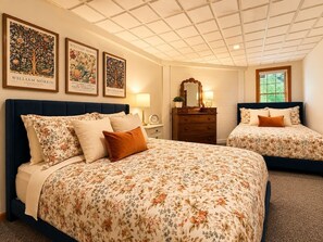 Ein Hotelzimmer mit einem großen Bett, einem kleineren Bett, einem Schminktisch und einem Spiegel. An der Wand hängen gerahmte Bilder.