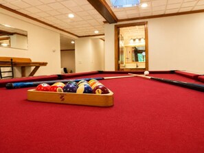 Ein Billardtisch mit Kugeln und Spielstangen, eine Holzbank und ein Spiegel in einem Raum mit gefliestem Himmel.