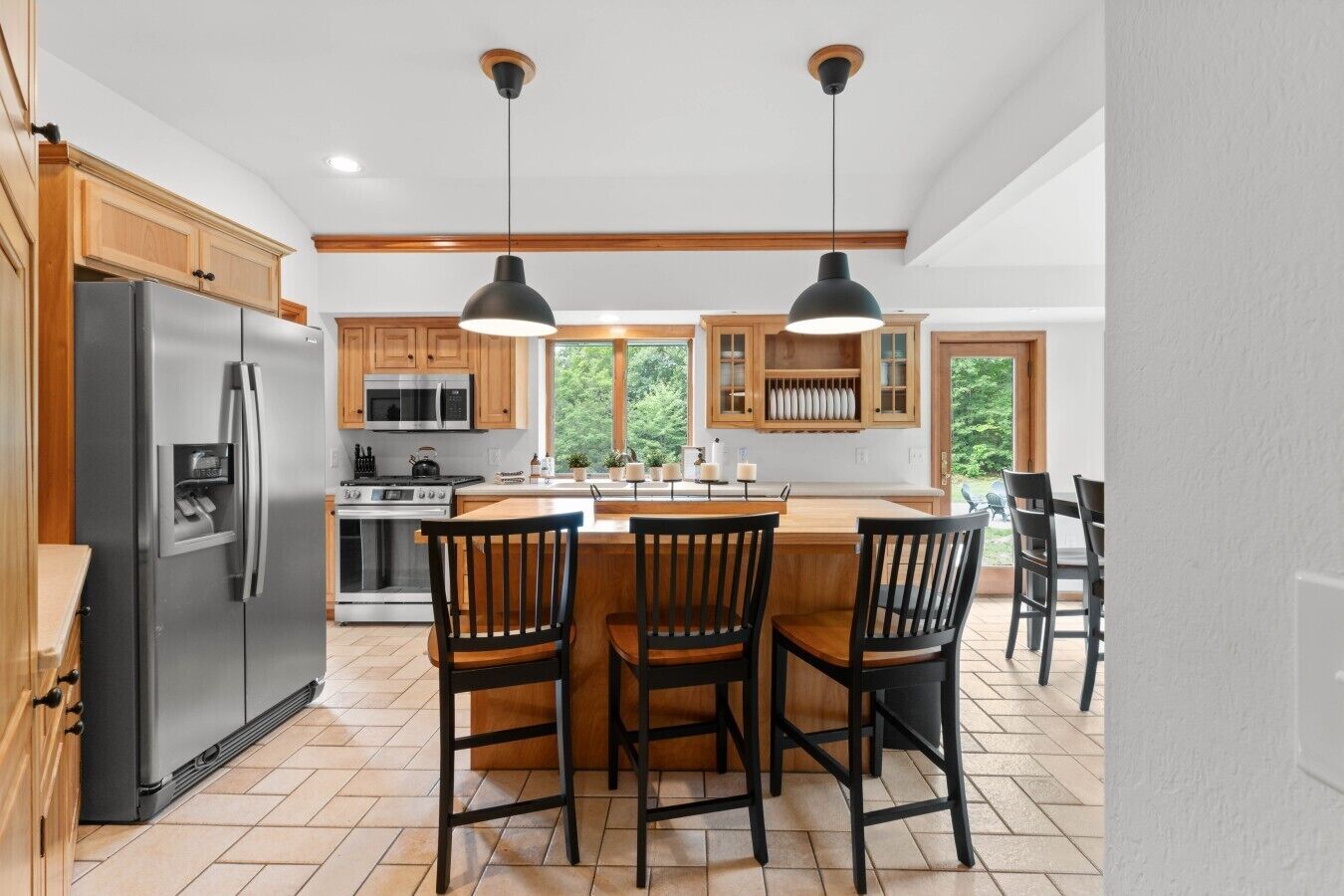 A kitchen with a central island, wooden cabinets, a stainless steel refrigerator, and pendant lighting.
