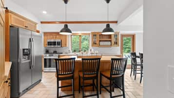A kitchen with a central island, wooden cabinets, a stainless steel refrigerator, and pendant lighting.