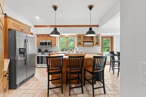 A kitchen with a central island, wooden cabinets, a stainless steel refrigerator, and pendant lighting. - Private 2-Acre Escape | Hot Tub • Fire Pit • Games (Bartlett)
