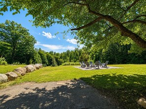 A picnic area with a table and chairs, surrounded by a grassy field and trees.