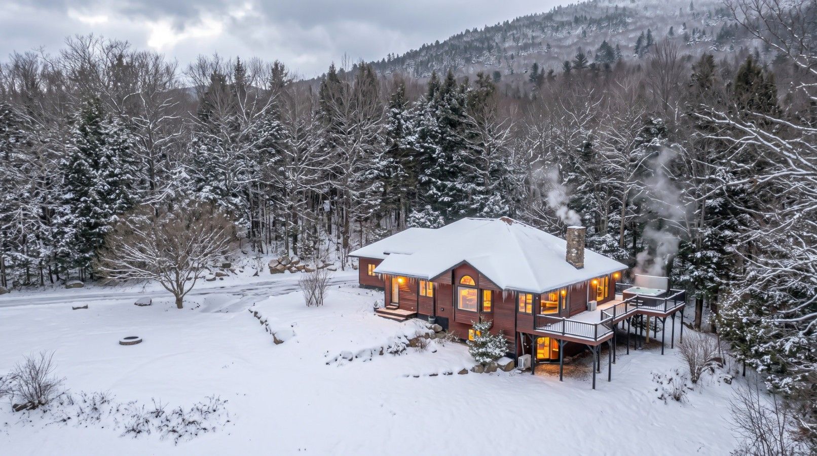 A snow-covered house with a chimney emitting smoke, surrounded by trees and a snowy landscape.