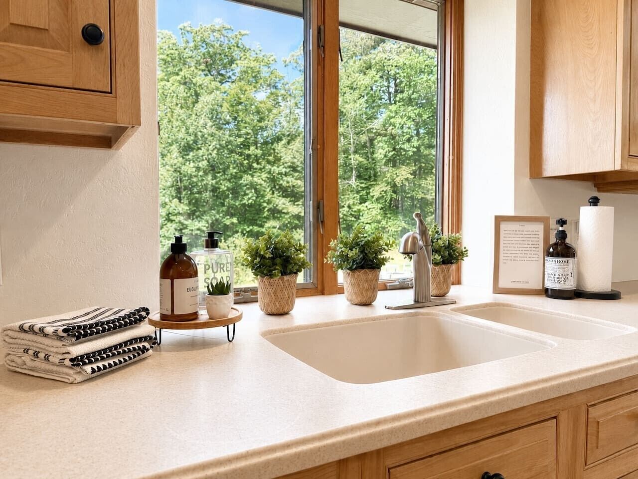 A kitchen with a large window, wooden cabinets, a sink, and various kitchen items.