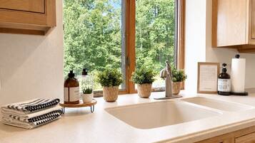A kitchen with a large window, wooden cabinets, a sink, and various kitchen items.