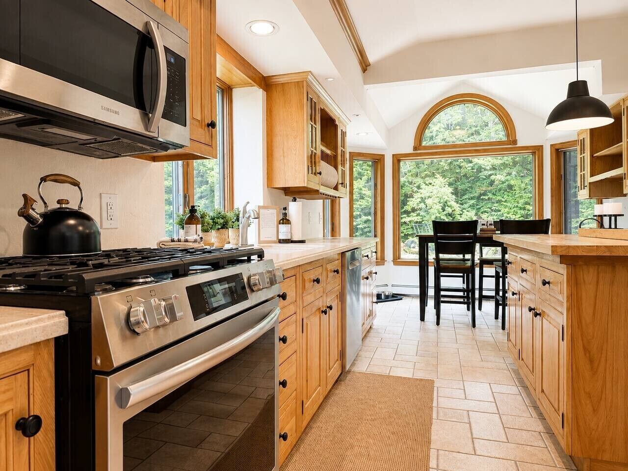 A modern kitchen with stainless steel appliances, wooden cabinetry, and a large window providing a view of the outdoors.