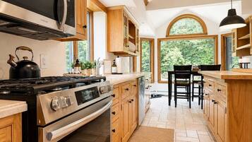 A modern kitchen with stainless steel appliances, wooden cabinetry, and a large window providing a view of the outdoors.