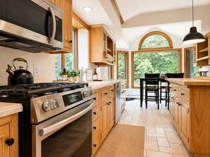 Une cuisine moderne dotée d’appareils électroménagers en acier inoxydable, de meubles de rangement en bois et d’une grande fenêtre offrant une vue sur l’extérieur.
