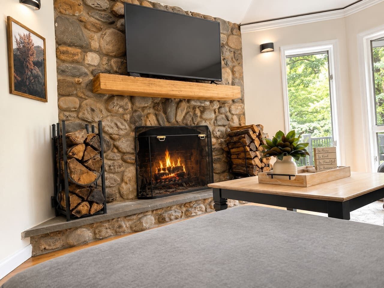A stone fireplace with a TV mounted above it, a wooden shelf, and a table with a plant and a sign with messages.