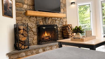 A stone fireplace with a TV mounted above it, a wooden shelf, and a table with a plant and a sign with messages.