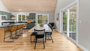 Uma cozinha moderna com uma ilha central, banquetas e uma mesa de jantar com cadeiras.