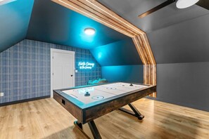 A room with a foosball table, a neon sign, and a sloped ceiling. - Rewind Retreat-King beds, Cinema, Hot tub, Dogs. (Conway)