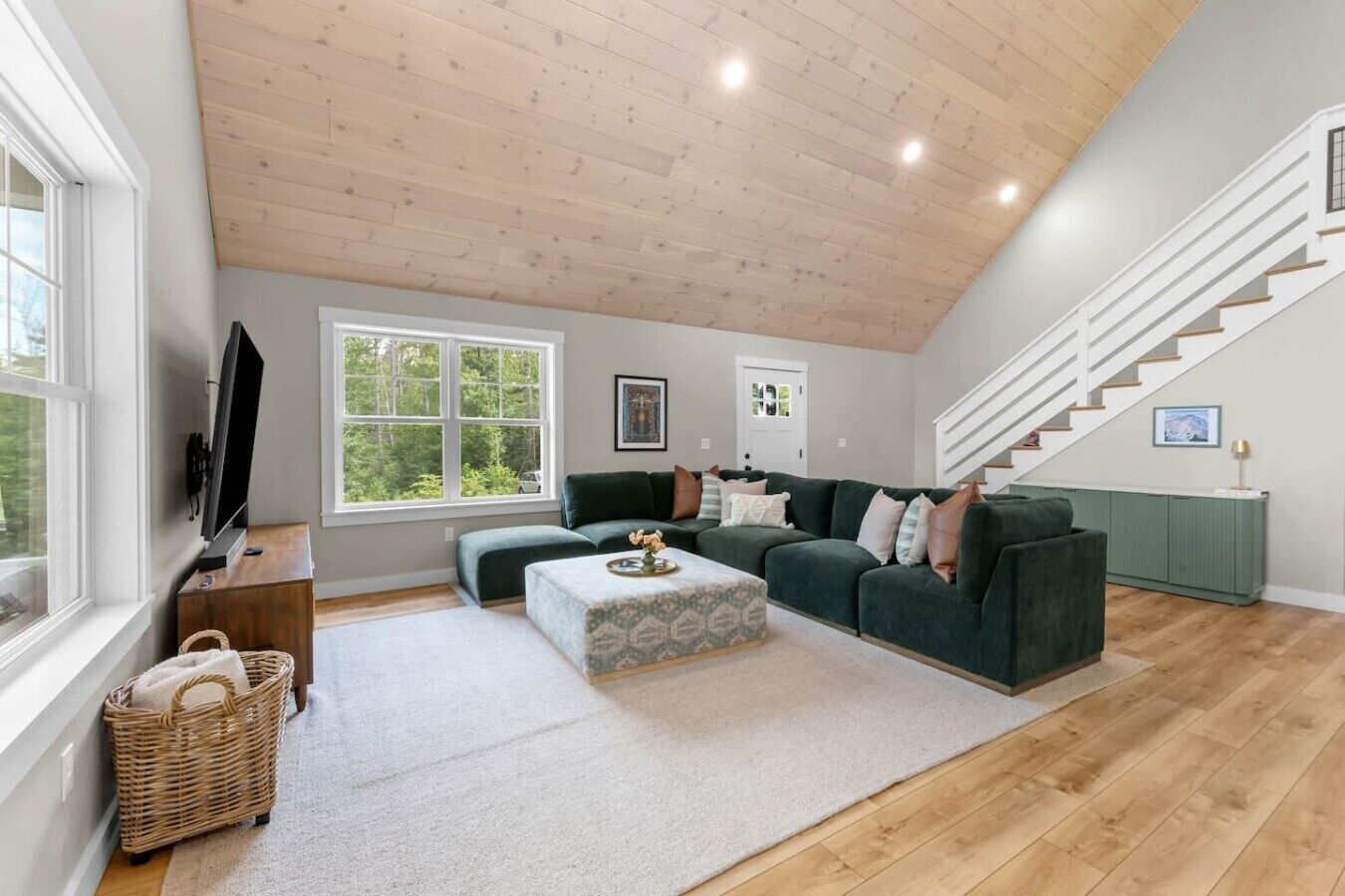 A spacious living room with a large sectional sofa, a flat-screen TV, a wooden ceiling, and a staircase.
