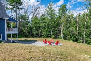 A house with a covered porch and a fire pit area with red chairs.