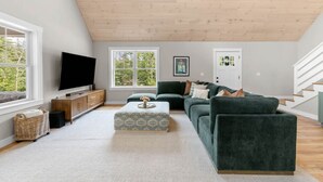 Uma sala de estar moderna com uma televisão de tela plana, um sofá verde, uma mesa de centro e teto de madeira.