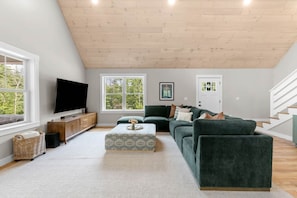 Ein modernes Wohnzimmer mit Flachbildfernseher, einem grünen Sofa, einem Couchtisch und einer Holzbalkendecke.