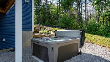 An outdoor hot tub with a stone surround, positioned on a gravel area adjacent to a building with blue siding.