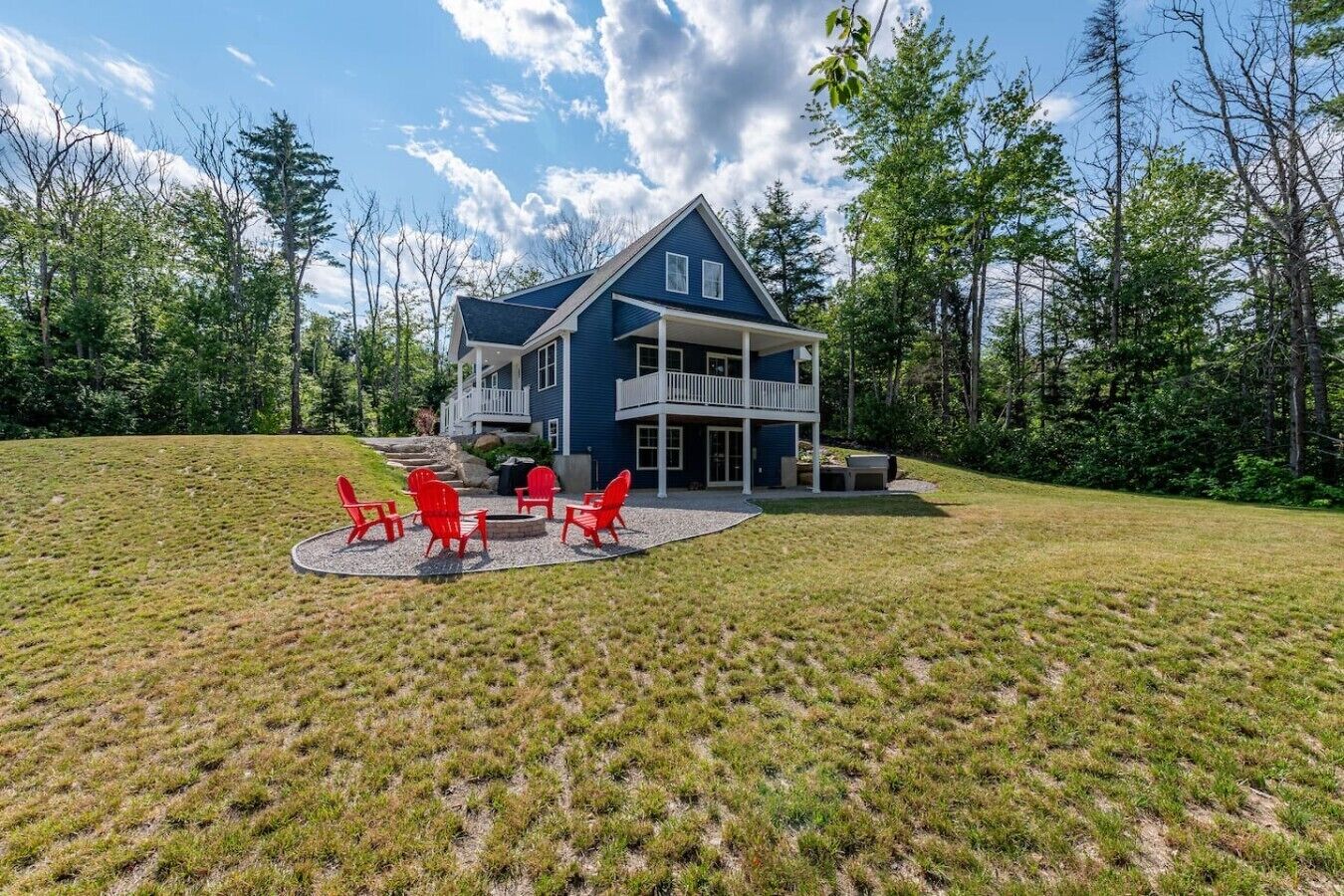 A two-story house with a covered patio and red chairs.