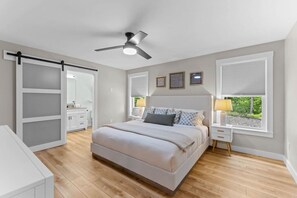 Ein Schlafzimmer mit einem Bett, einem Deckenventilator, einem Fenster mit Jalousien und einem Nachttisch mit Lampe.