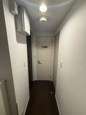 A narrow hallway with a white door at the end, a light fixture on the ceiling, and a small vent on the wall. - Kyoto 2-Bedroom Apartment | 40 sqm | Free Parking | Sleeps 5 | Nozomi 202 (Kyoto-shi Minami-ku)