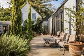 A wooden deck with outdoor furniture, surrounded by greenery and a building with large windows. - Peaceful Coastal Escape near Beach (Cowes)