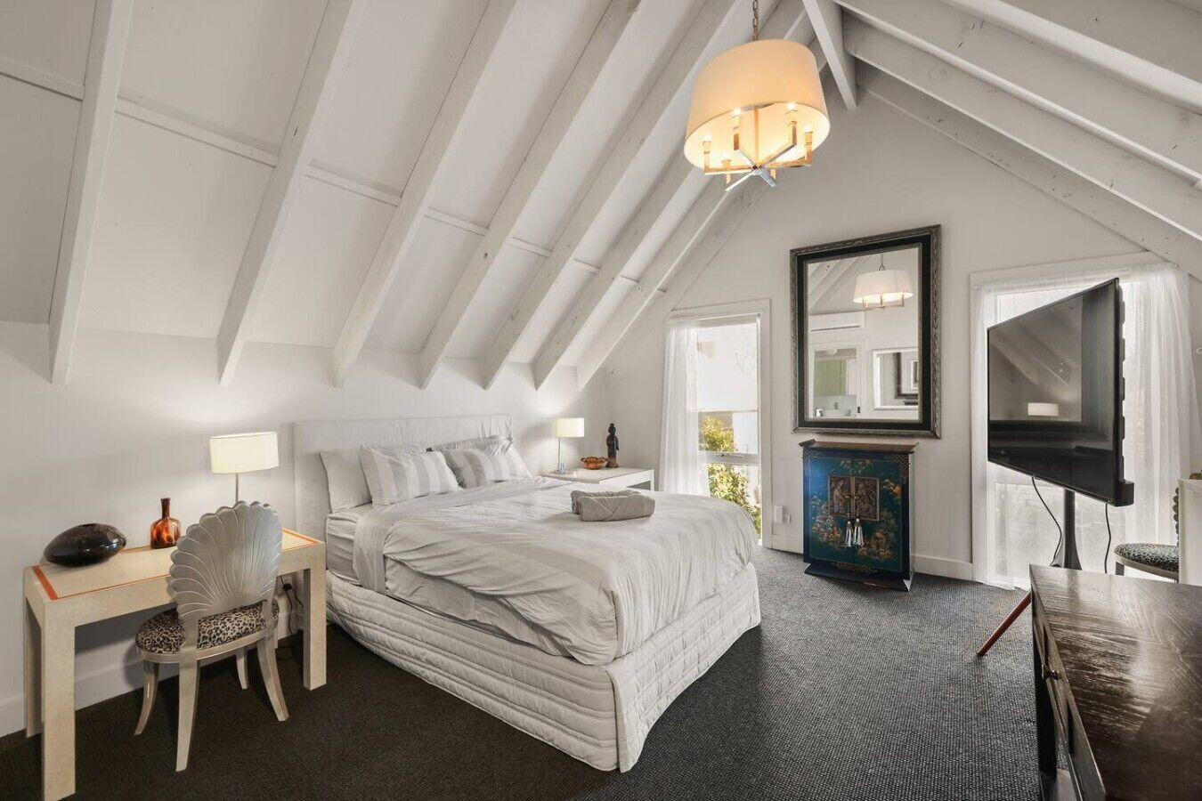 A bedroom with a large bed, a desk, a chair, a television, and a mirror.