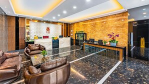 Un hall de hotel con mostrador de recepción, asientos de cuero, suelo de mármol y una pared decorativa.