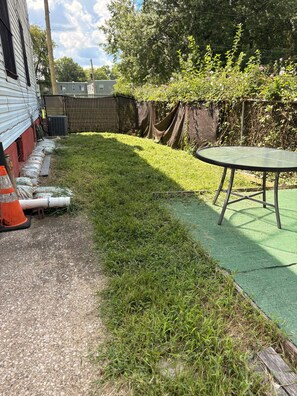 A backyard with a green artificial turf, a metal table, and a row of bags along a gravel path. - 3-bedroom house in adorable Philadelphia with cool AC breeze near Phila airport (Philadelphia)